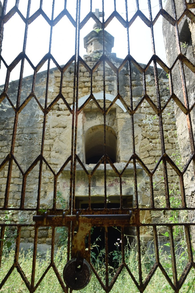 An abandoned and forgotten chapel with weeds and a padlocked gate